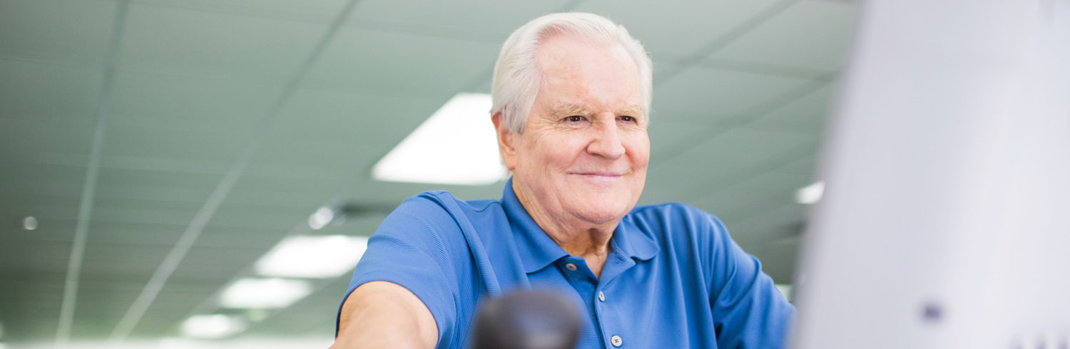 Smiling elderly man exercising at a gym.