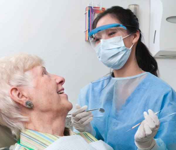 Masked dentist with older woman