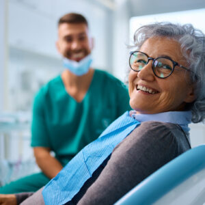 Happy senior woman at dental clinic looking at camera. Her dentist is in the background.