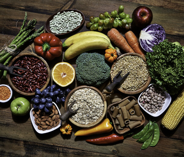 Dietary and healthy food themes. Table top view of fresh vegetables and legumes on rustic wooden table. Food is rich of fiber ideal for dieting and healthy eating. Includes corn, avocado, broccoli, orange fruit, grapes, bell pepper, lettuce, banana, apple almonds and wholegrain pasta.